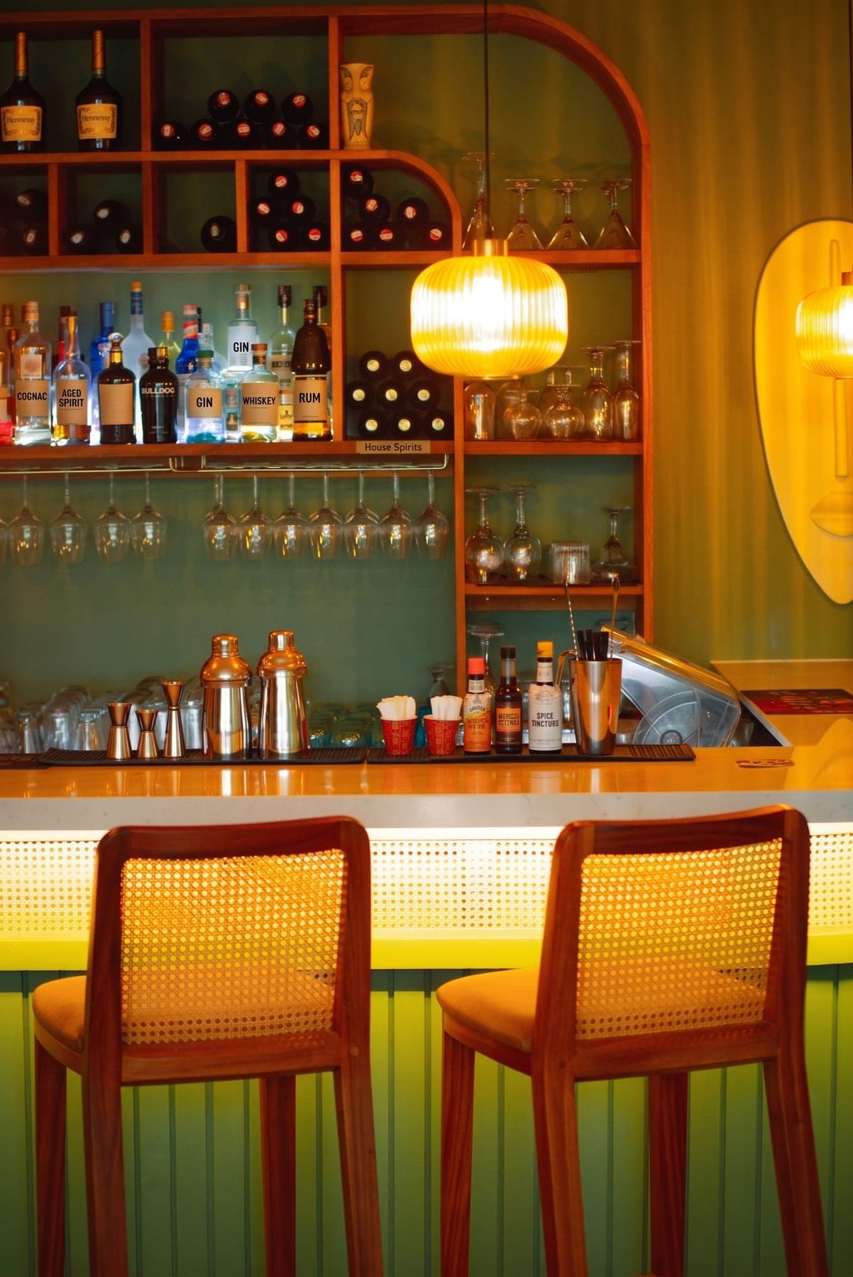 A bar counter at service, spirits shelf and glassware behind, stools waiting. Where the brand is chosen out loud.