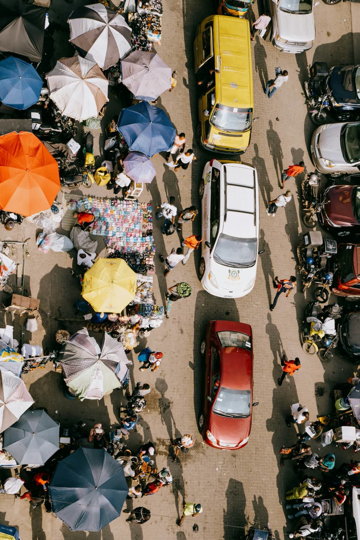 A Lagos market from above: stalls, umbrellas and traffic threading between them.