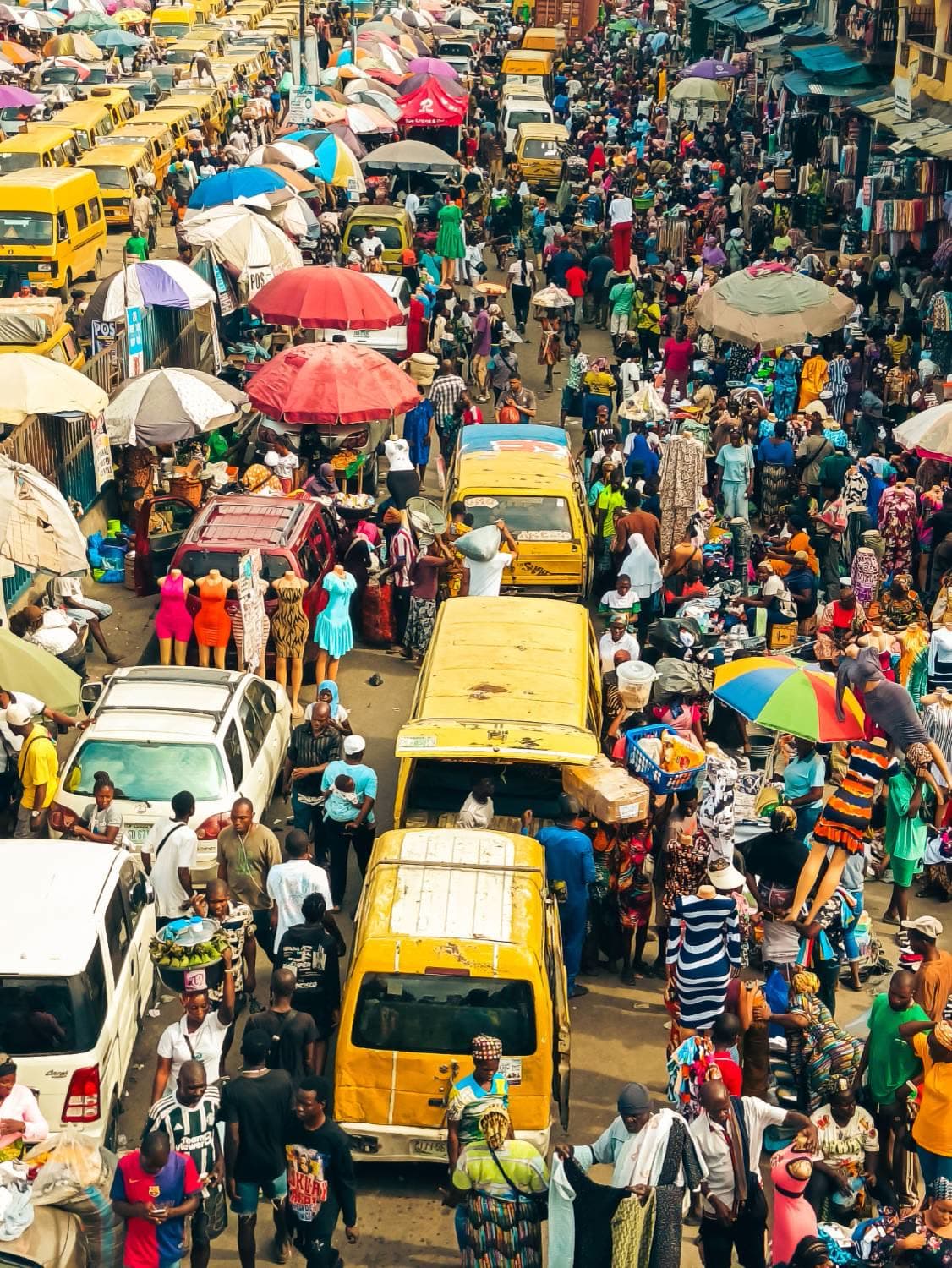 A Lagos market street at rush hour — danfo buses, traders, umbrellas, the crowd the brand is being judged by.